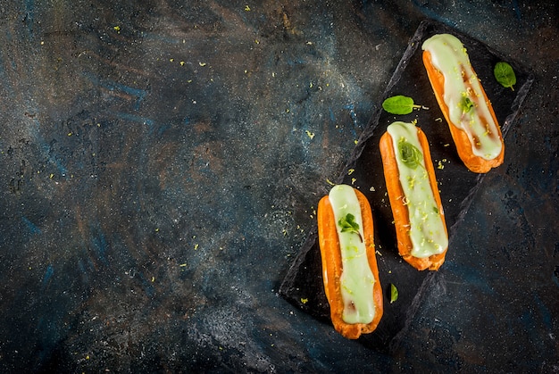 Zdjęcie tradycyjny francuski deser. mojito eclairs z skórką limonki i liśćmi mięty, na ciemnoniebieskim, widok z góry copyspace