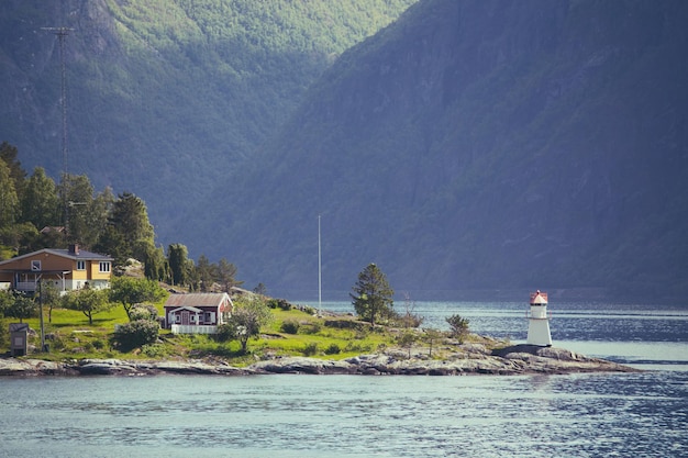 Tradycyjny norweski czerwony drewniany dom do postawienia nad jeziorem w pobliżu latarni morskiej i gór w oddali, norwegia