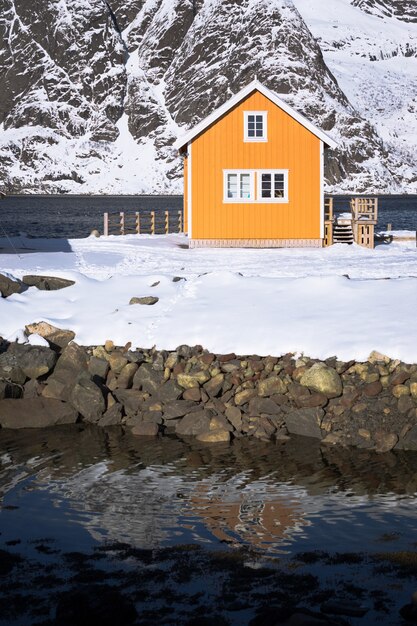 Tradycyjny norweski drewniany dom rorbu do stania na brzegu fiordu i gór w oddali. Lofoty. Norwegia.