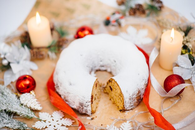 Tradycyjny okrągły bożonarodzeniowy stollen z bakalii posypany cukrem pudrem na tle świątecznego wystroju ze świecami. Tradycyjne świąteczne ciastko.