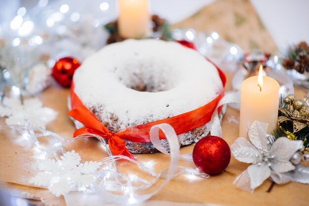 Tradycyjny Okrągły Bożonarodzeniowy Stollen Z Bakalii Posypany Cukrem Pudrem Na Tle świątecznego Wystroju Ze świecami. Tradycyjne świąteczne Ciastko.
