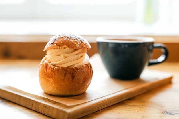 Zdjęcie tradycyjny słodki bułeczek semla z pastą migdałową z biczowaną śmietaną i filiżanką czarnej kawy