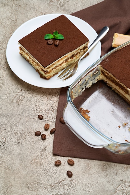 Tradycyjny włoski deser tiramisu w szklanym naczyniu do pieczenia Savoiardi ciasteczka i porcja na szarym betonowym stole