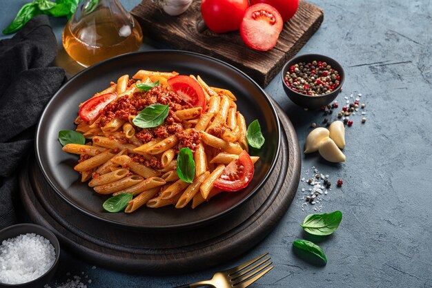 Tradycyjny włoski makaron boloński z bazylią i pomidorami na grafitowym tle z miejscem do kopiowania. Widok z boku.