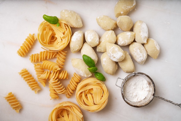 Tradycyjny włoski makaron: tagliatelle, fusilli i gnocchi ozdobione liśćmi bazylii. Koncepcja kuchni włoskiej. Widok z góry. Flat Lay