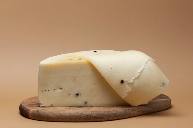 Tradycyjny włoski ser Caciotta z dodatkiem czarnego pieprzu. Połowa głowy sera na drewnianej desce.