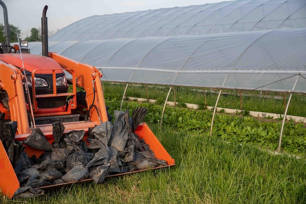 Zdjęcie traktor farmy pomarańczowej z workami z piaskiem w ekologicznej szklarni warzywnej