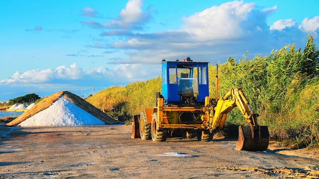 Traktor i hałdy soli w stawie odparowywania soli w Marsala, wyspa Sycylia, Włochy