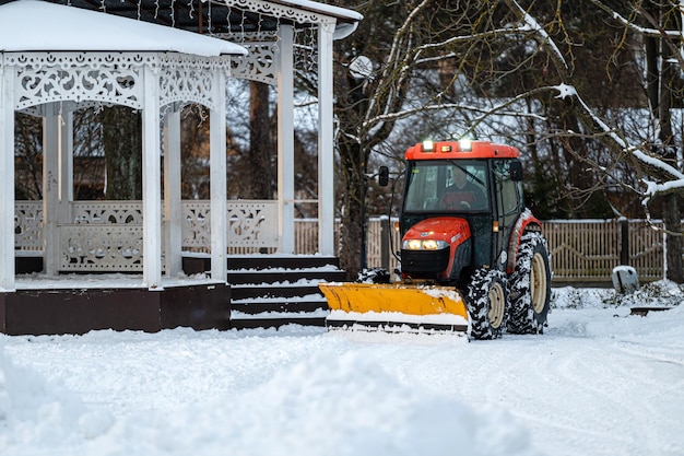 Traktor odśnieżający odśnieża teren w parku Służba komunalna sprząta chodnik ze śniegu