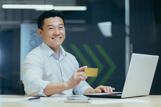 Transakcje finansowe kartą kredytową młody azjatycki mężczyzna pracujący w biurze przy laptopie i używający
