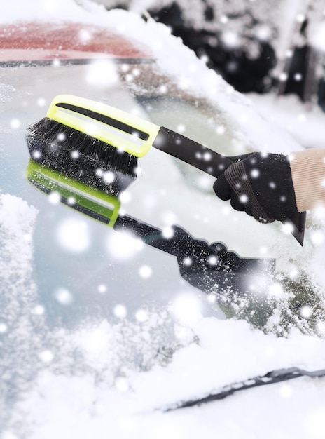 transport, zima, pogoda, koncepcja ludzi i pojazdów - zbliżenie człowieka czyszczącego śnieg z przedniej szyby samochodu za pomocą pędzla