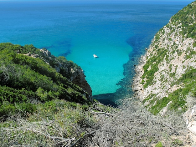 Trawa na skalistym klifie z białą łodzią zacumowaną na błękitnych wodach morskich na Formenterze w Hiszpanii