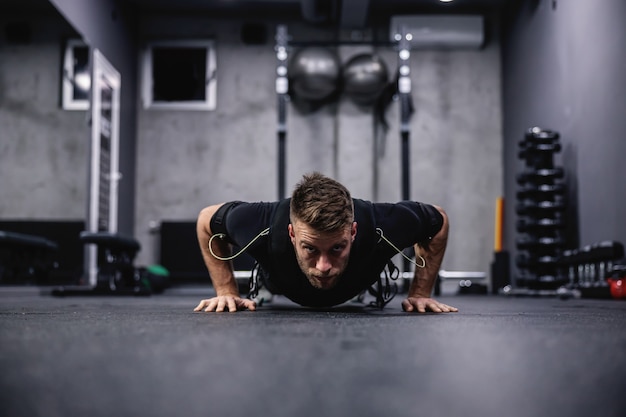 Trener fitness w specjalnym garniturze dla technologii EMS, wykonujący ćwiczenia ramion i klatki piersiowej oraz pompki w nowoczesnej koncepcji siłowni. Rewolucja w treningu, rehabilitacji ciała