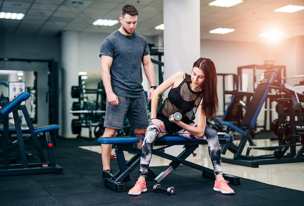 Trener i klient ćwiczą na siłowni z hantle Młoda brunetka z osobistym trenerem fitness Koncepcja fitness Zbliżenie Selektywna ostrość