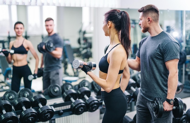 Trener i klient patrząc w lustro podczas treningu na siłowni z hantlami Młoda brunetka z osobistym trenerem fitness Koncepcja fitness Zbliżenie Selektywna ostrość