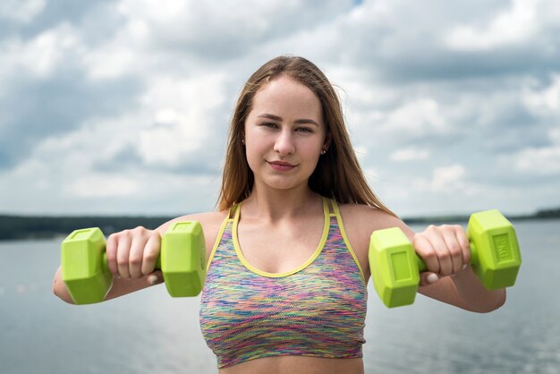 Trener lekkoatletycznego fitness młodych ćwiczeń z hantlami na plaży nad jeziorem. Zdrowy tryb życia