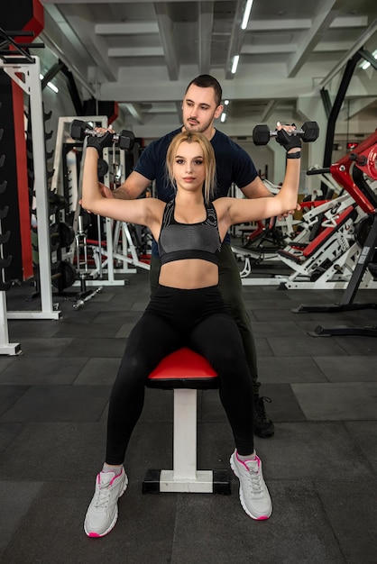 Trener mężczyzny pomaga jej szczupłej klientce ćwiczyć z ciężkimi hantlami na siłowni Fitness i siłownia dla koncepcji zdrowia