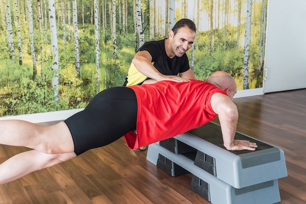 Trener personalny pomagający mężczyźnie robić pompki na podłodze na siłowni
