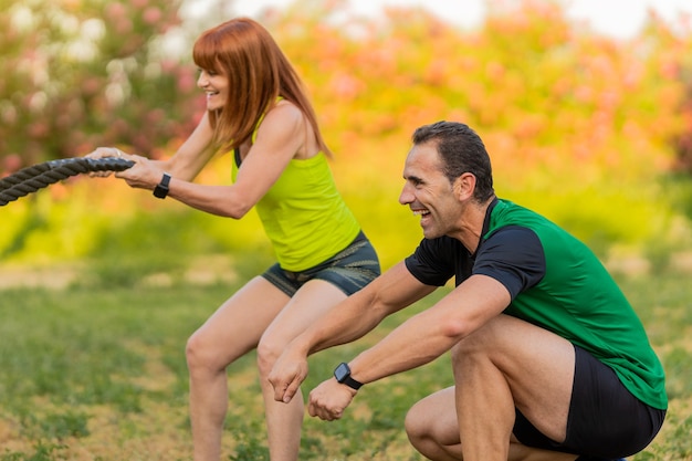 Trener Szczęśliwy Fitness Z Kobietą W Parku I Za Pomocą Liny Bojowej.