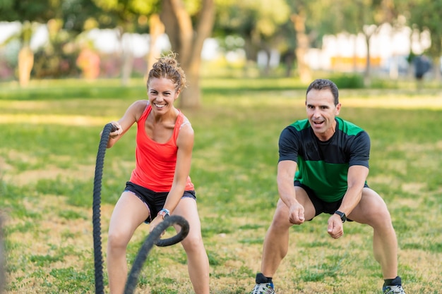 Trener szczęśliwy fitness z kobietą w parku i za pomocą liny bojowej.