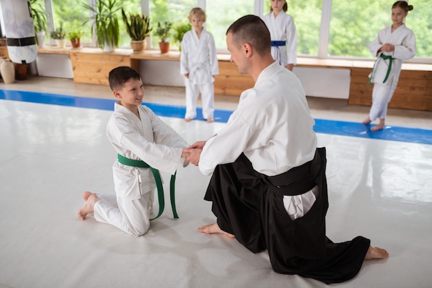 Trener uścisk dłoni. Trener aikido ściska dłonie swojego małego ucznia, jednocześnie wspierając go przed treningiem