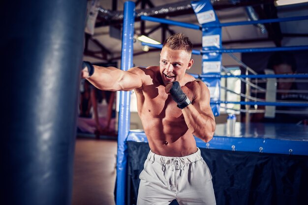 Trening Boksera Z Workiem Bokserskim W Ciemnej Hali Sportowej. Trening Młodych Bokserów Na Worek Treningowy.