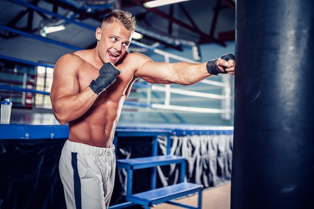 Trening boksera z workiem bokserskim w ciemnej hali sportowej. Trening młodych bokserów na worek treningowy.