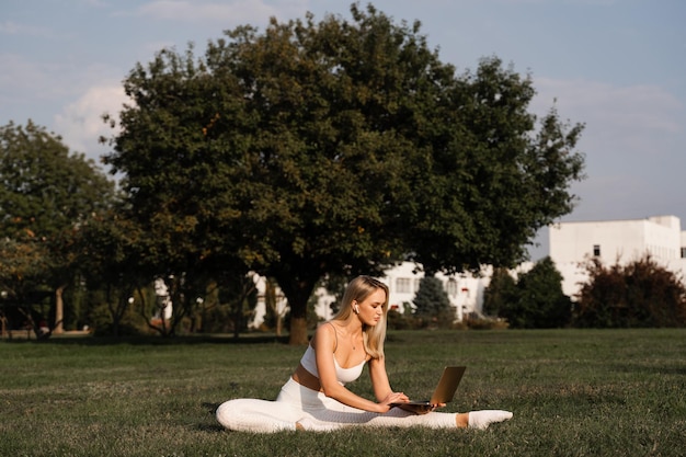 Trening Fitness Online Z Laptopem W Parku Wysportowana Blondynka Siedzi Na Trawie I Rozmawia Z Trenerem Sportowy Styl życia Na świeżym Powietrzu