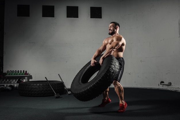 Trening sportowy Muskularny mężczyzna przerzucanie opony na siłowni