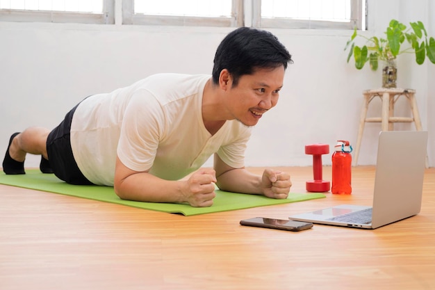 Trening w domu Wysportowany mężczyzna robi deskę do jogi podczas oglądania samouczka online na laptopie