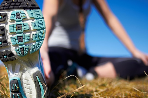 Zdjęcie trening zbliżenia podeszwy buta i miejsce na makietę przez rozmyte tło z kobietą rozciągającą nogi trampki powiększają i makiety do biegania odnowy biologicznej lub ćwiczeń z dziewczyną na trawie dla zdrowego treningu