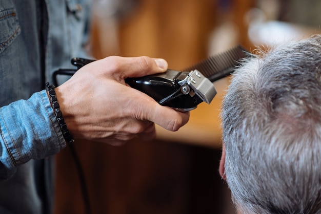 Trochę po bokach. Widok z tyłu starszego siwowłosego mężczyzny przycinanego przez fryzjera w zakładzie fryzjerskim.