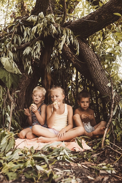 Troje wiejskich dzieci bawi się w chatce, którą sami zbudowali z liści i gałązek