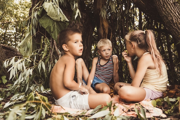 Troje wiejskich dzieci bawi się w chatce, którą sami zbudowali z liści i gałązek