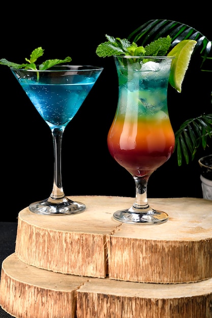 Trójkolorowy kieliszek koktajlowy obok szklanki z napojem z błękitnej laguny na czarnym tle