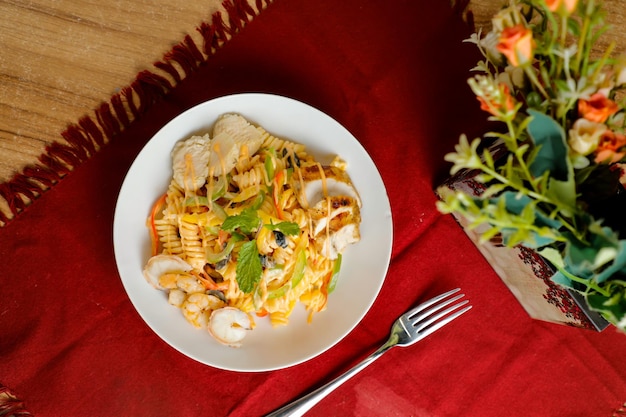 Tropical Pasta Salad With Mix Mięso oliwka z krewetkami i krewetkami podawane w misce z kwiatami i widelcem izolowanym na czerwonej serwetce boczny widok zdrowego zielonego jedzenia na stole