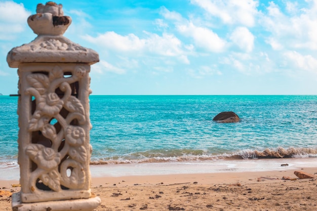 Tropikalna piaszczysta plaża z kamienną dekoracyjną kolumną i błękitnym morzem w słoneczny dzień Podróże i turystyka