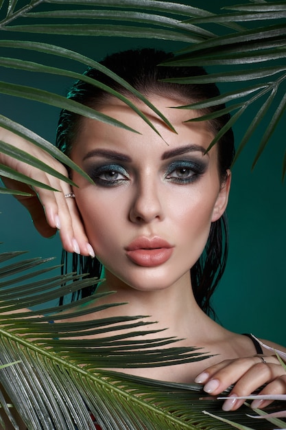 Tropikalny portret sexy kobieta w liście palmy. Jasny zielony makijaż, cień liści palmowych na twarzy dziewczyny. Piękny makijaż