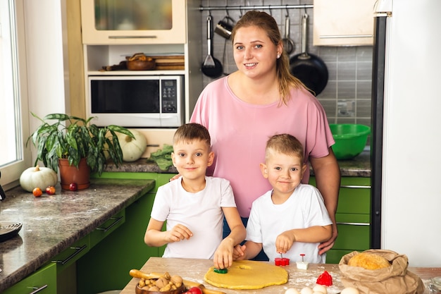 Troskliwa Mama Pomaga Małym Synom W Wieku Przedszkolnym Przygotować Ciasteczka, Uśmiechnięta Kochająca Mama Uczy Się Gotowania Z Małym Dzieckiem, Robiąc Razem Obiad W Weekend W Kuchni