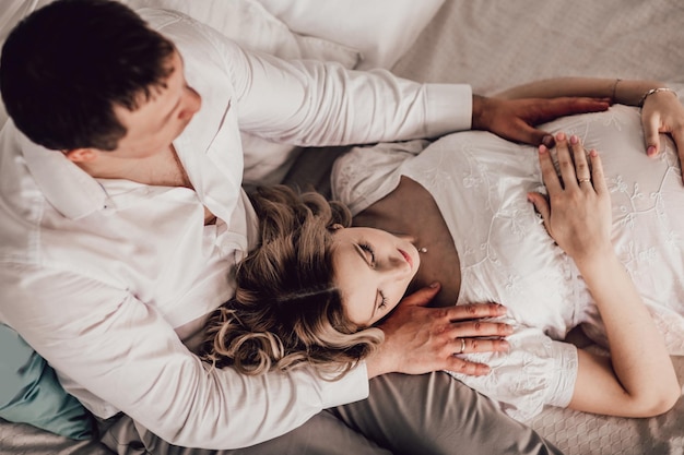 Troskliwy mąż przytula swoją ciężarną żonę siedząc na łóżku.