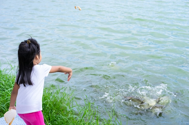 Troszkę dziewczyny karmienia ryba przy stawowym parkiem publicznie