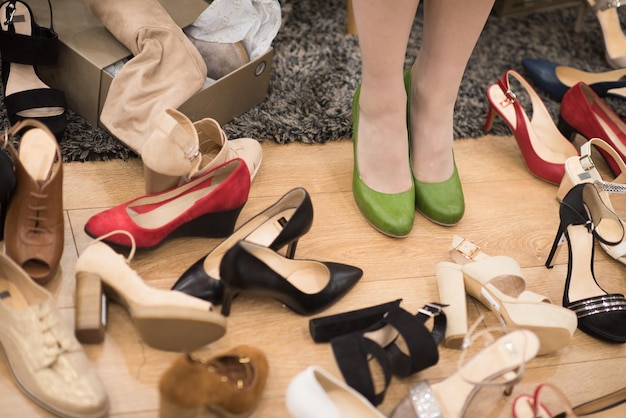 Trudny wybór. Zbliżenie: młoda kobieta siedzi w sklepie obuwniczym, podczas gdy obok niej leżą różne buty