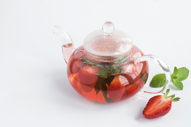 Truskawkowa herbata w szklanym czajniczku na białym tle. Zdrowy napój. Zbliżenie.