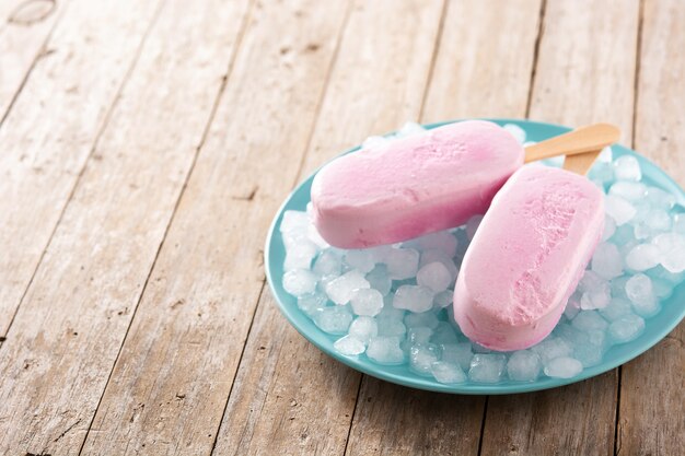 Truskawkowe popsicles i kruszony lód na niebieskim talerzu na drewnianym stole