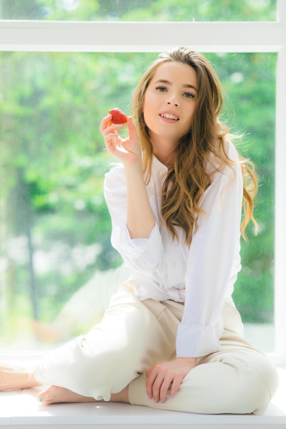 Truskawkowe usta Piękna młoda kobieta bez koszuli trzymająca truskawkę w dłoni i degustująca