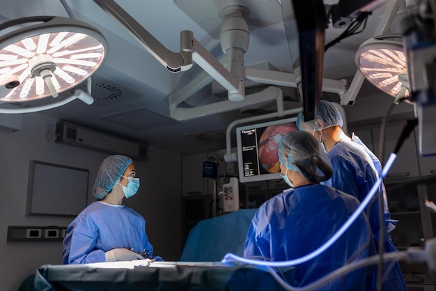 Trzech chirurgów wykonujących operację laparoskopową Lekarze patrzący na obraz na monitorze Koncepcja medycyny i opieki zdrowotnej Narząd wewnętrzny pacjenta widziany na monitorze komputera