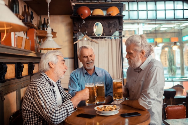 Trzech emerytów. Trzech siwych emerytów w podeszłym wieku jedzących przekąski i pijących piwo