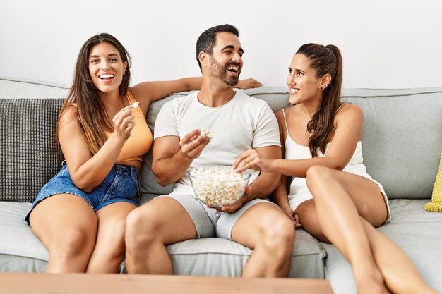 Trzech latynoskich przyjaciół oglądających film siedzący na kanapie w domu.