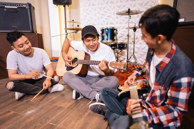 Trzech młodych Azjatów grających razem na gitarze, siedząc na podłodze