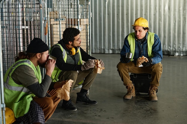 Trzech młodych międzykulturowych inżynierów w odzieży roboczej rozmawiających w przerwie na lunch
